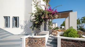 A white building with stone walls, a wooden pergola, and a small patio area with a table and chairs.