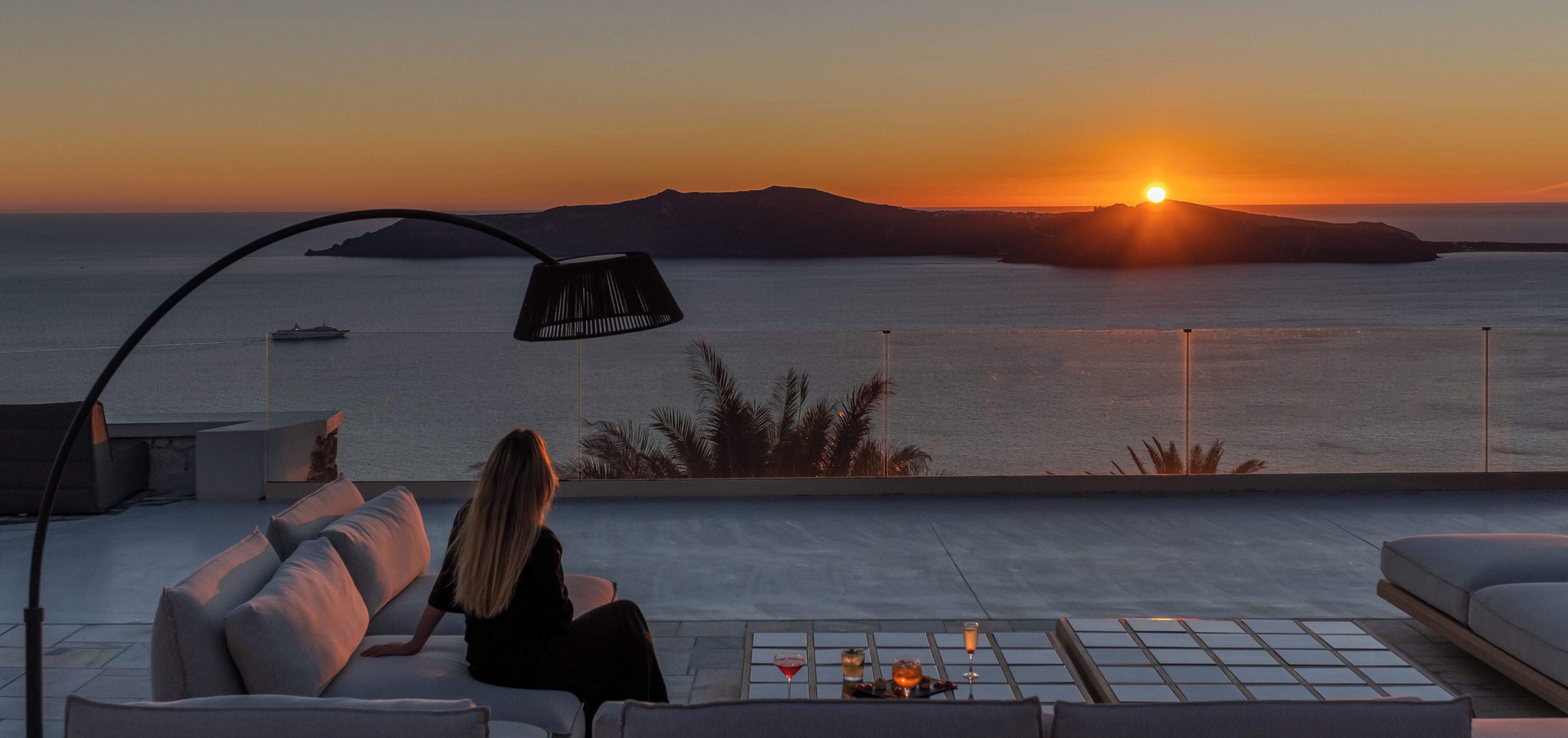 A person sitting on a sofa with a view of the sea and sunset.