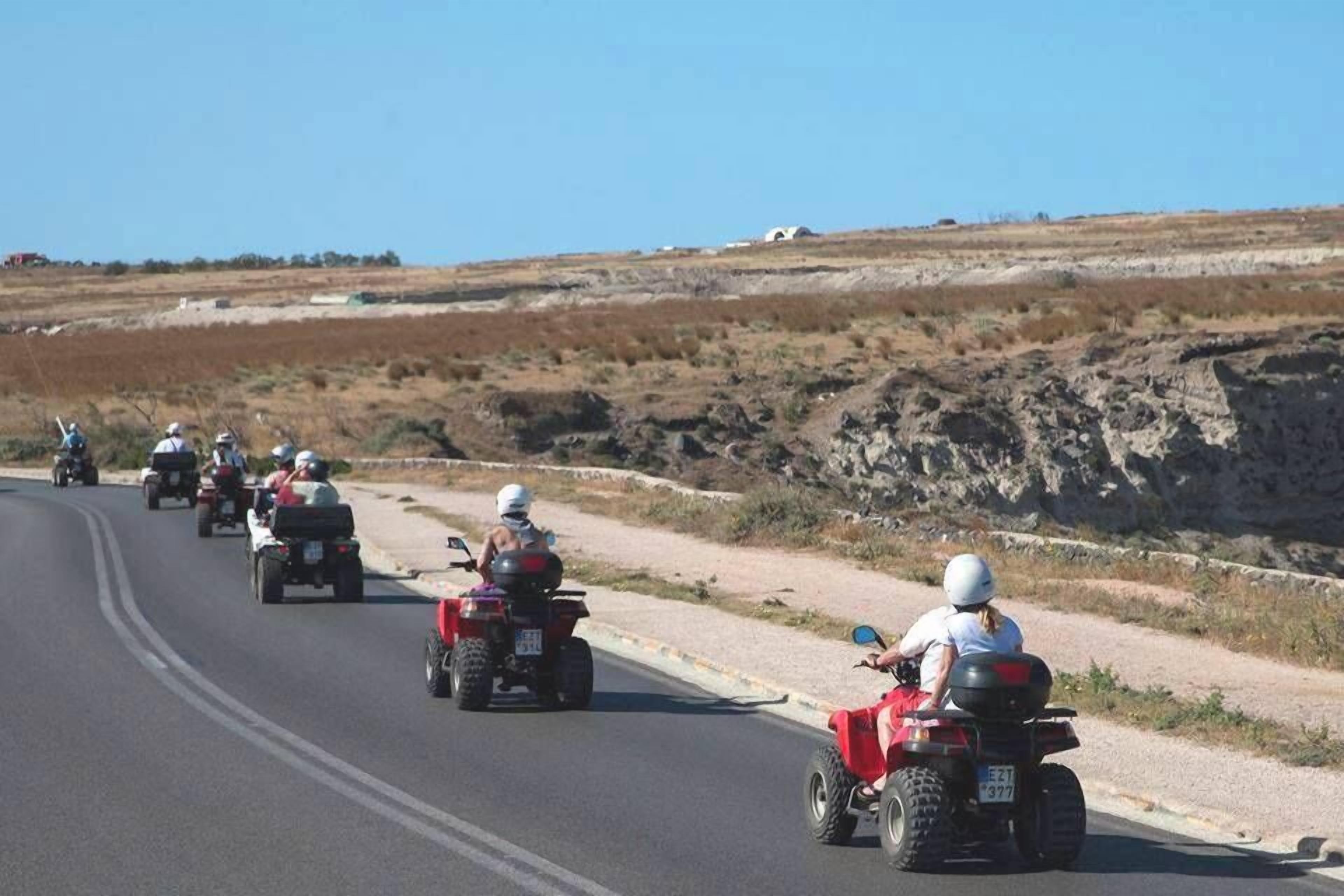 A group of people riding ATVs on a road with a hilly landscape in the background.