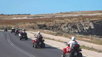 A group of people riding ATVs on a road with a hilly landscape in the background.