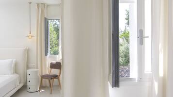 A modern bedroom with a white bed, a wooden chair, a bedside table, and a window with curtains.