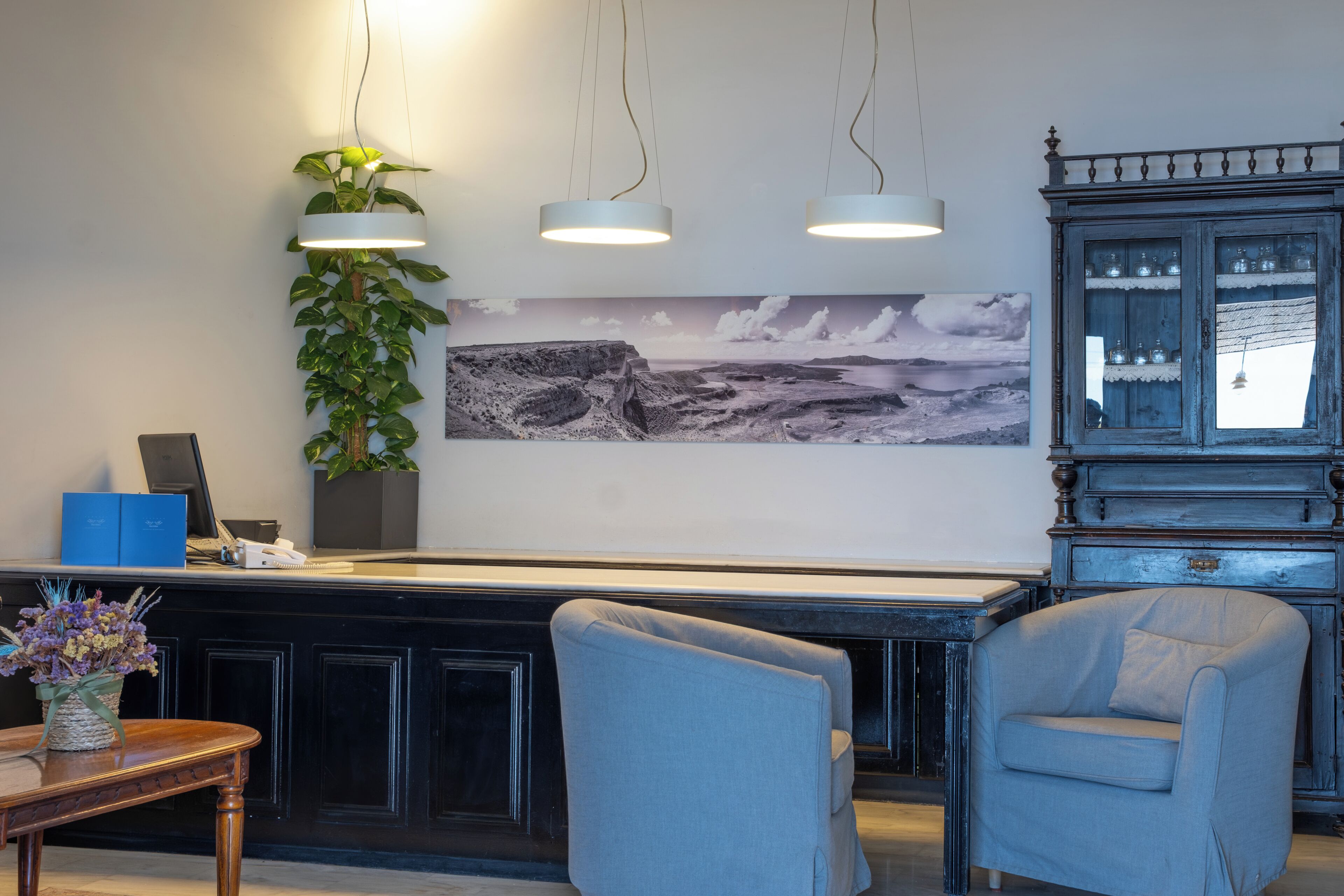 A reception area with a desk, two chairs, a potted plant, a wall-mounted lamp, and a framed landscape painting.