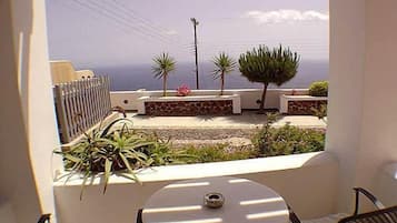 Un balcon avec une table et des chaises, donnant sur un jardin planté et offrant une vue sur la mer.