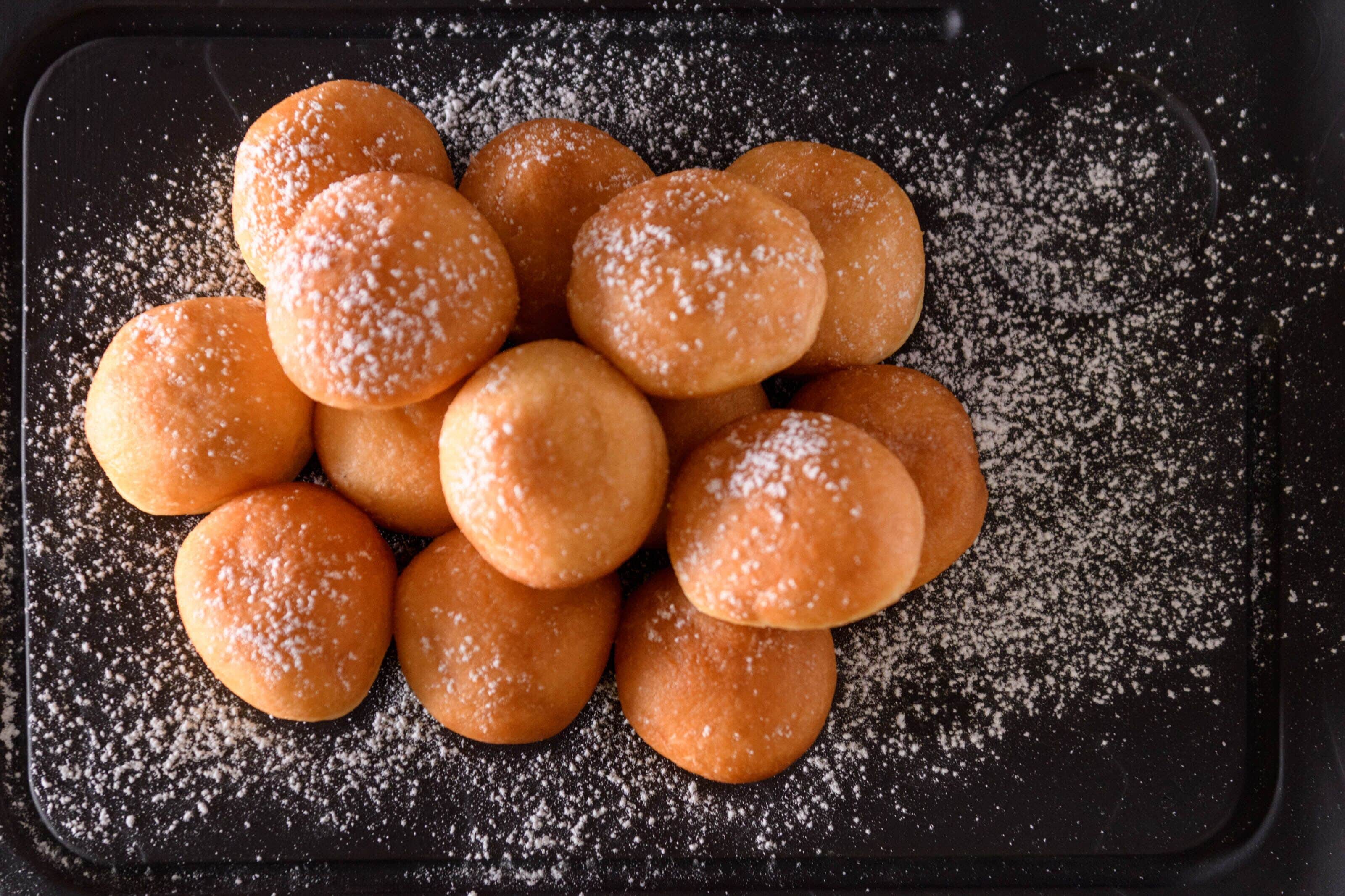 A tray of round, golden-brown pastries dusted with powdered sugar.
