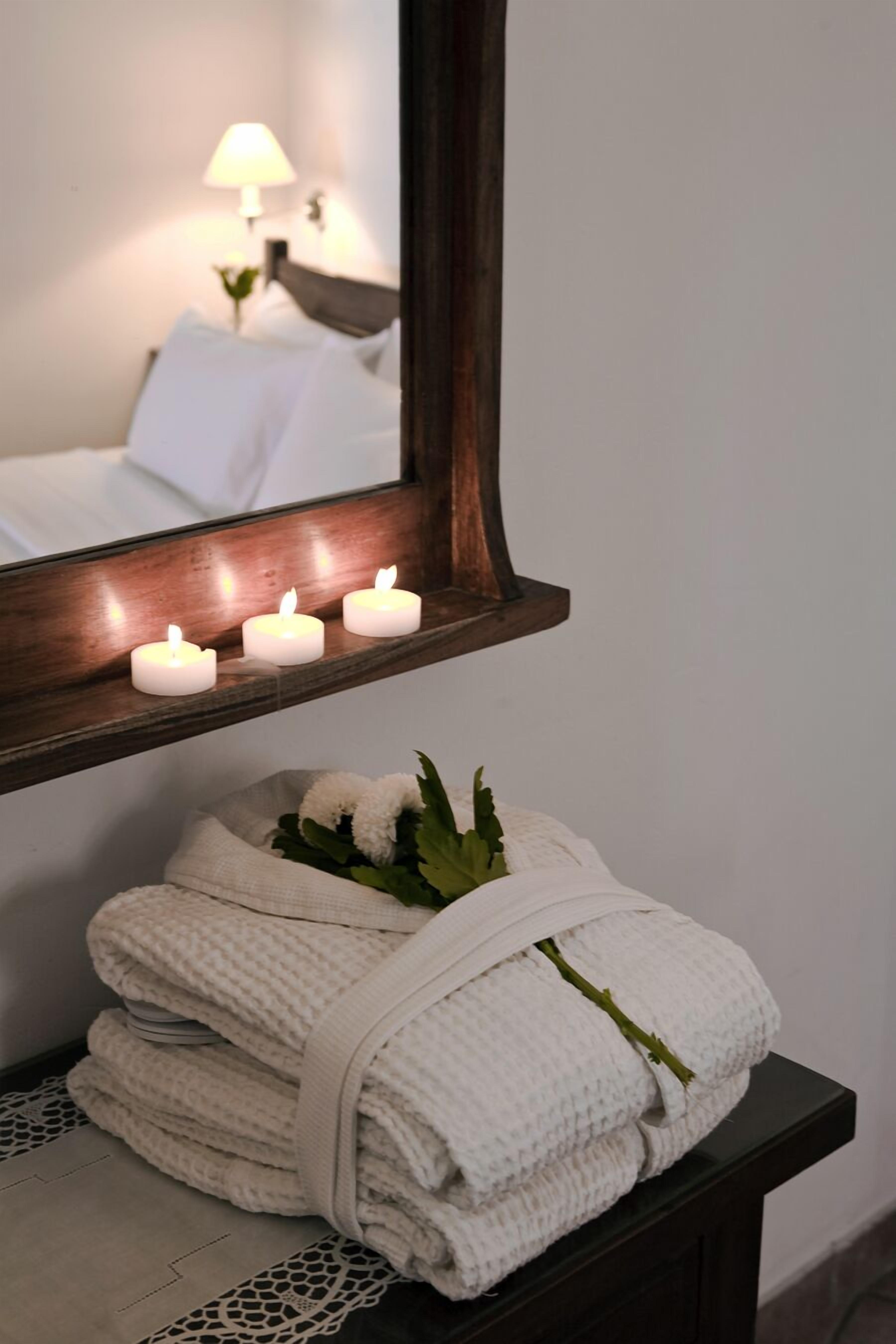 A bathroom with a mirror, four lit candles, and a stack of folded towels.