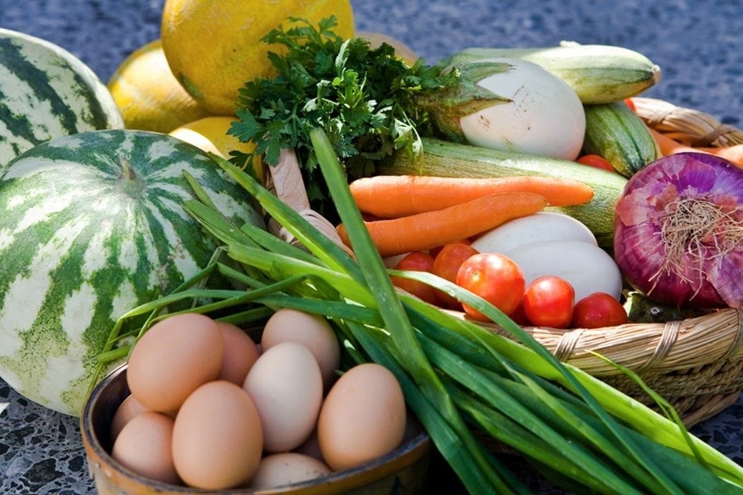 A variety of fresh produce including watermelon, carrots, tomatoes, onions, and eggs.