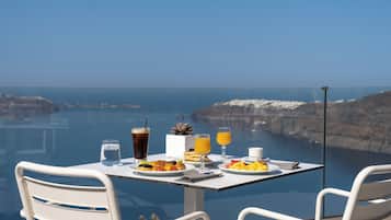 A dining table with plates of food, drinks, and a potted plant, overlooking a coastal landscape.