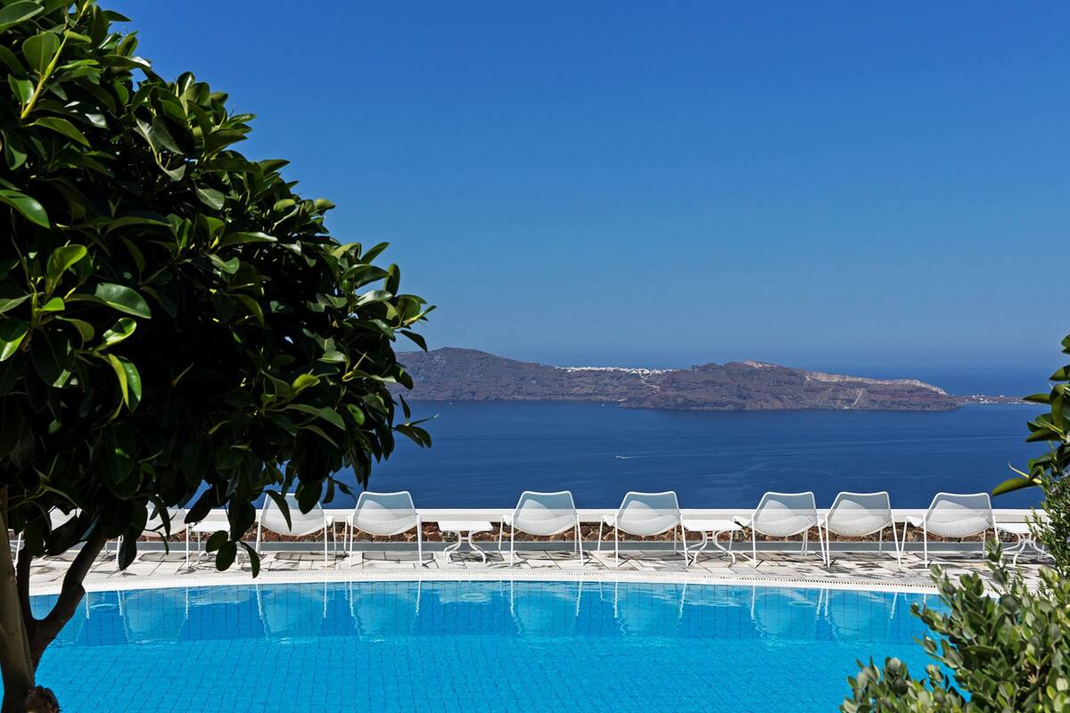 A pool with white lounge chairs and a view of a coastline.