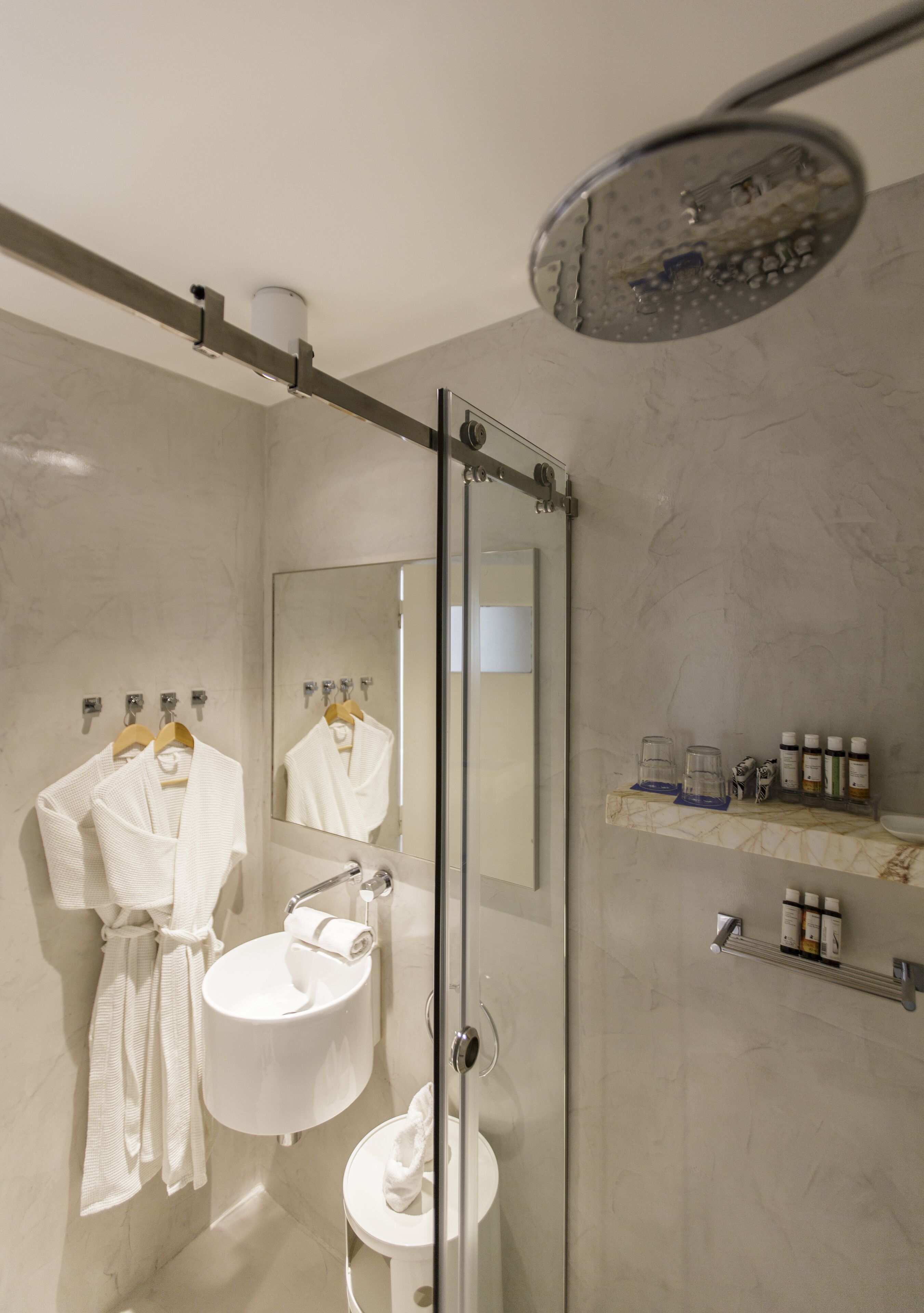Un baño moderno con cabina de ducha de vidrio, un lavabo con espejo y un mueble de tocador con artículos de aseo.