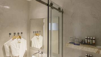 Un baño moderno con cabina de ducha de vidrio, un lavabo con espejo y un mueble de tocador con artículos de aseo.