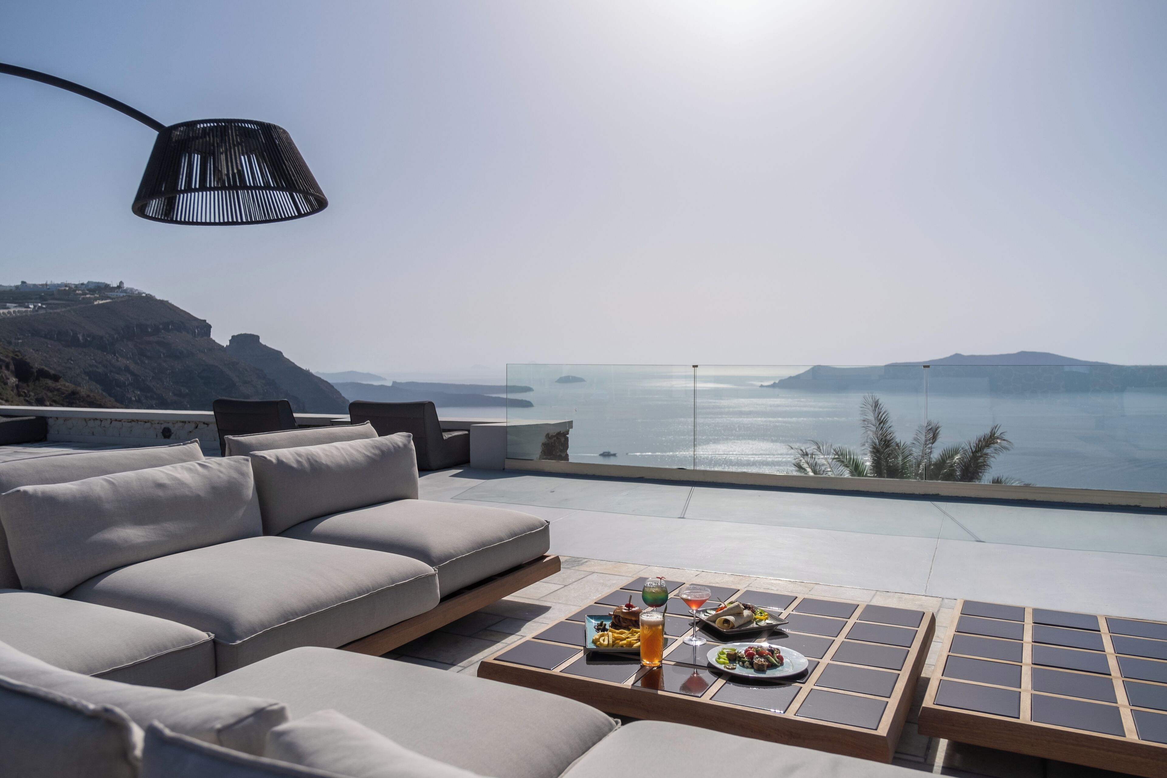 A modern outdoor seating area with a sofa and a table set for dining, overlooking a scenic body of water.