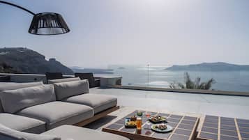 A modern outdoor seating area with a sofa and a table set for dining, overlooking a scenic body of water.
