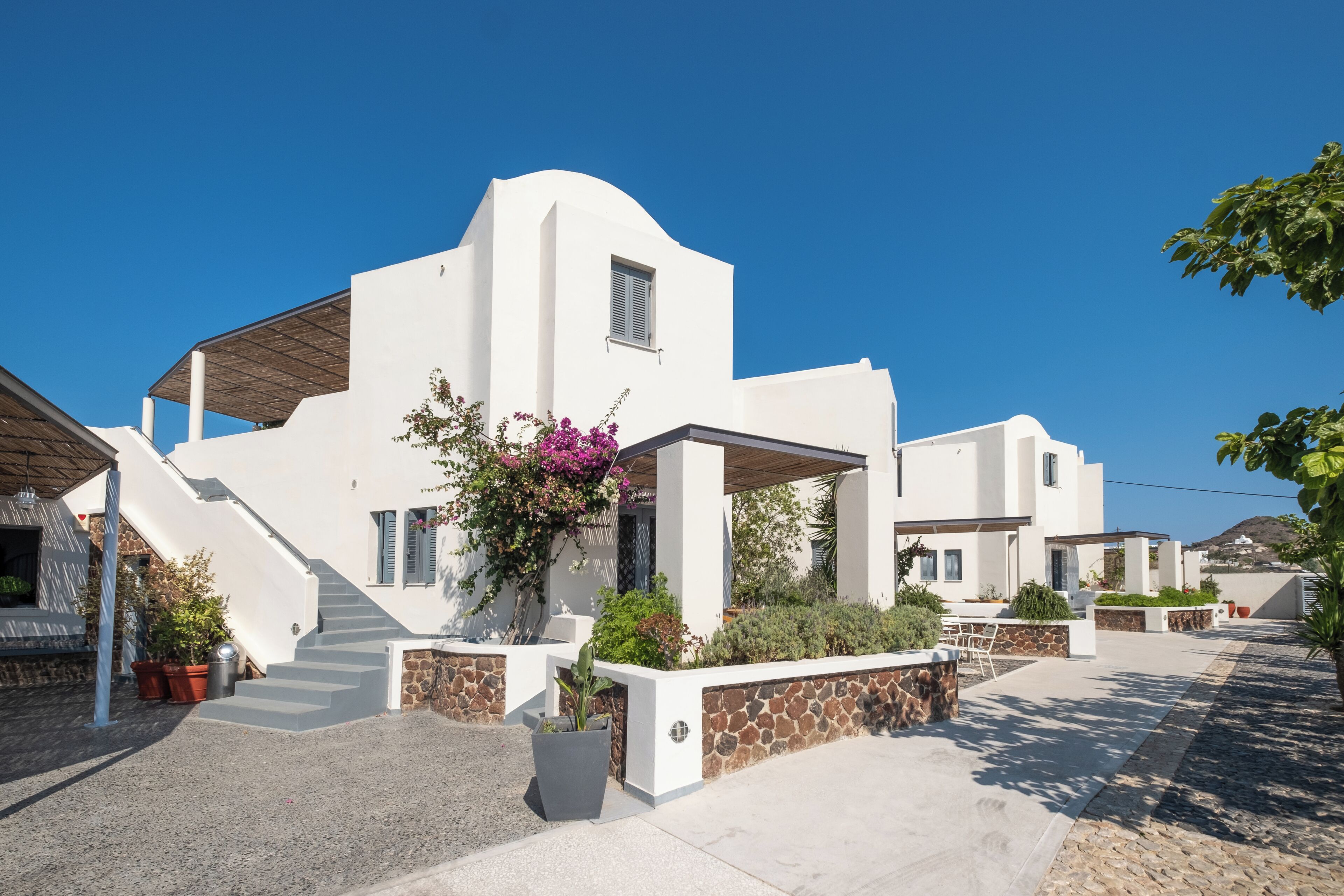 A modern white building with a stone facade, a covered outdoor area, and a staircase leading to the entrance.