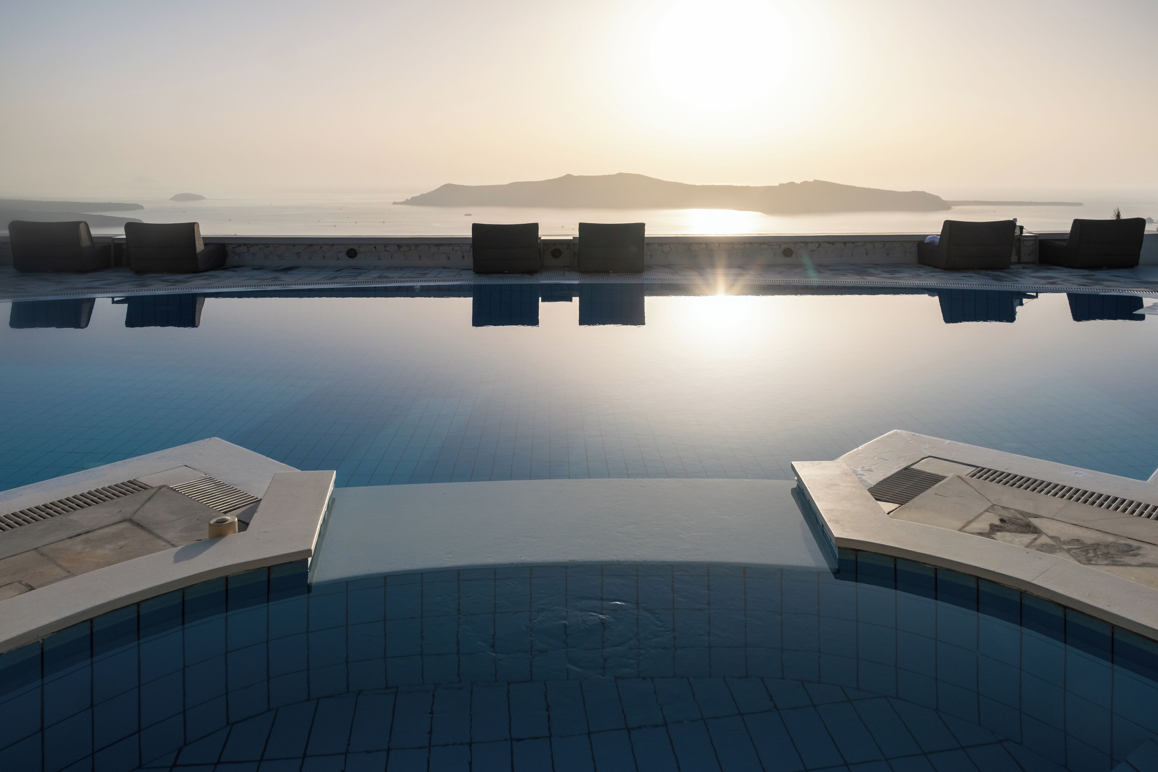 A pool with a view of the sea and a distant mountain at sunrise.