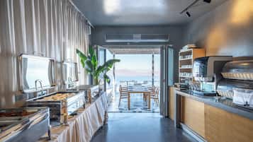 A modern kitchen with a buffet setup, a dining area with tables and chairs, and a view of the sea.