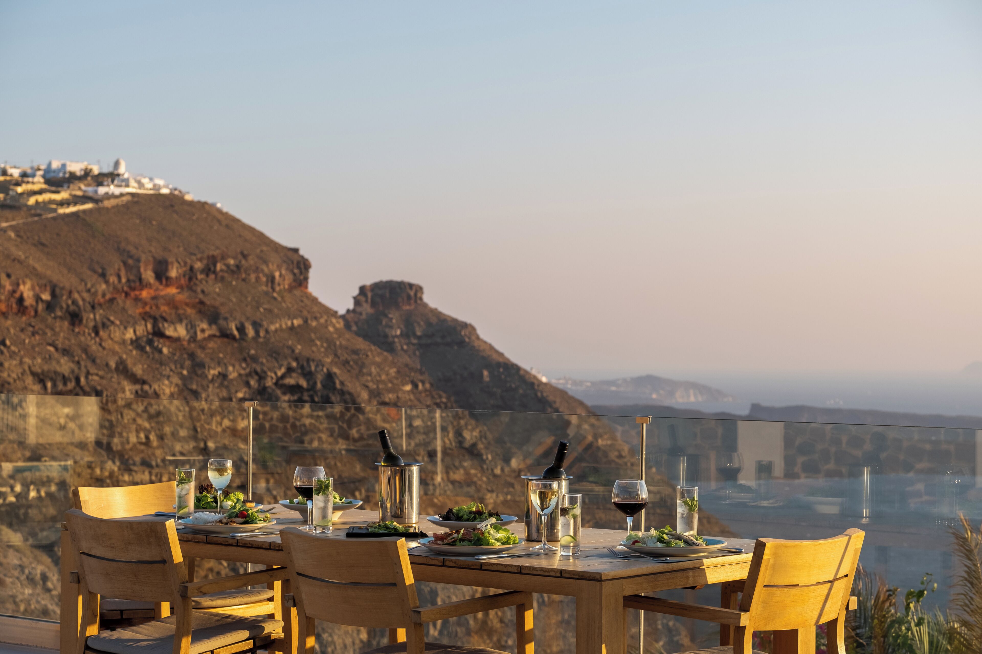 A dining table set with plates, glasses, and cutlery, overlooking a mountainous landscape.