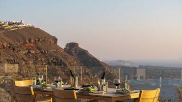 A dining table set with plates, glasses, and cutlery, overlooking a mountainous landscape.
