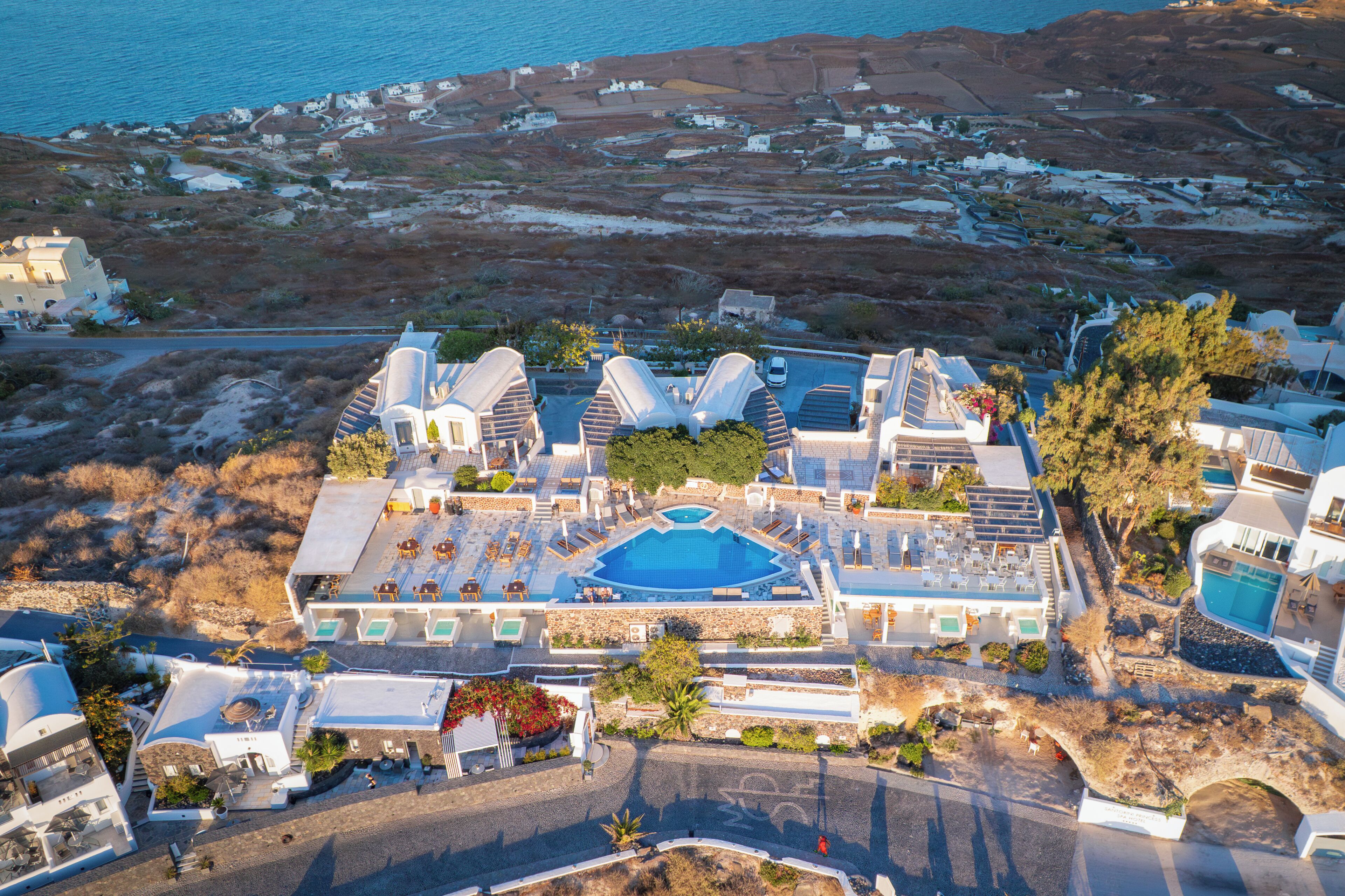 A resort with a central swimming pool, multiple guest rooms, and a view of the surrounding landscape.