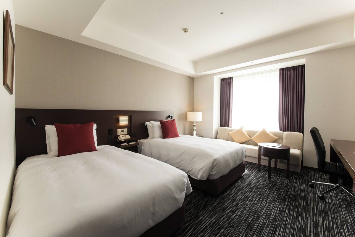 Ein Hotelzimmer mit zwei Betten, einer Sitzecke, einem Schreibtisch und einem Sessel.