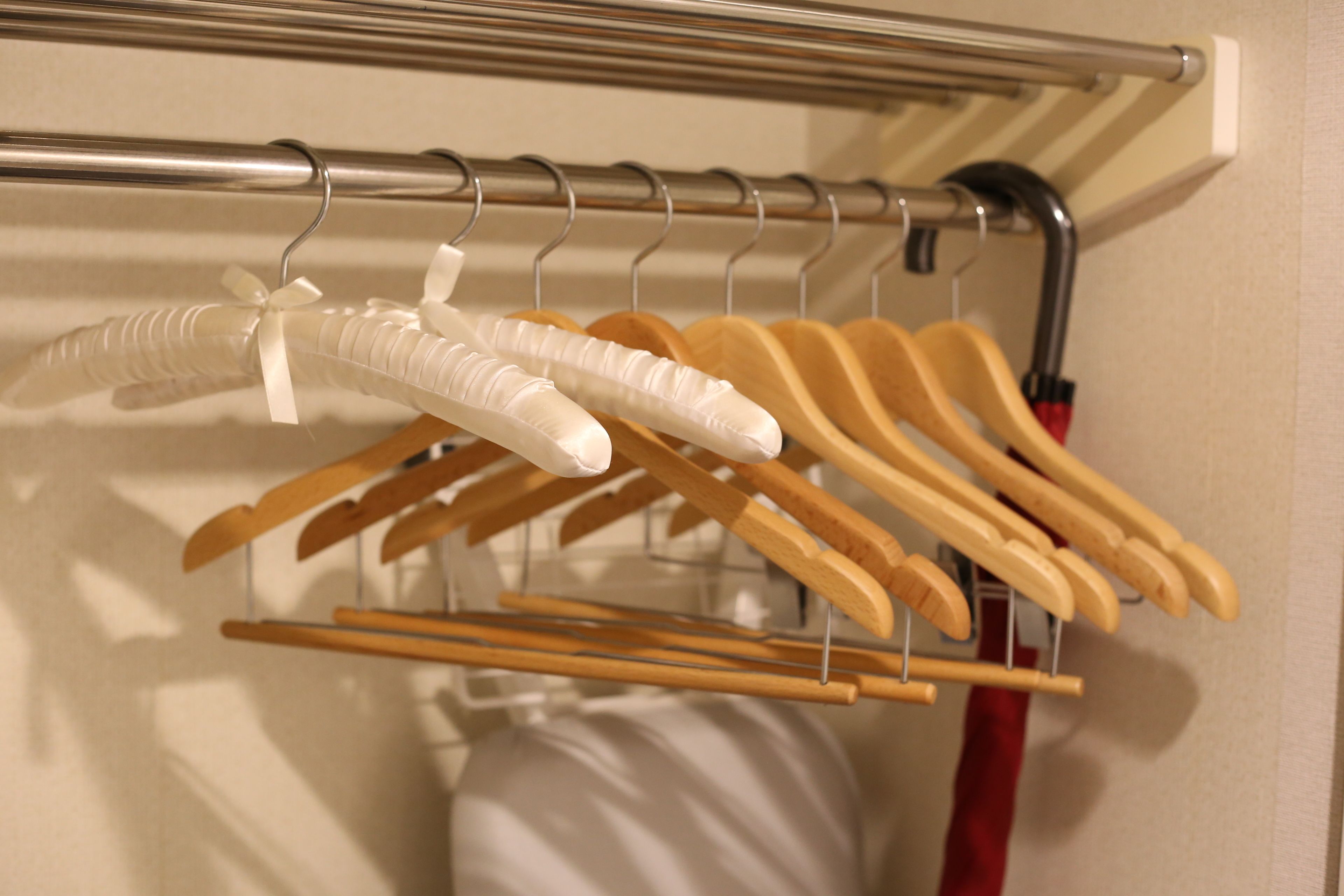 A clothing rack with various hangers, including wooden and plastic ones, in a room with a white wall and a red object in the background.