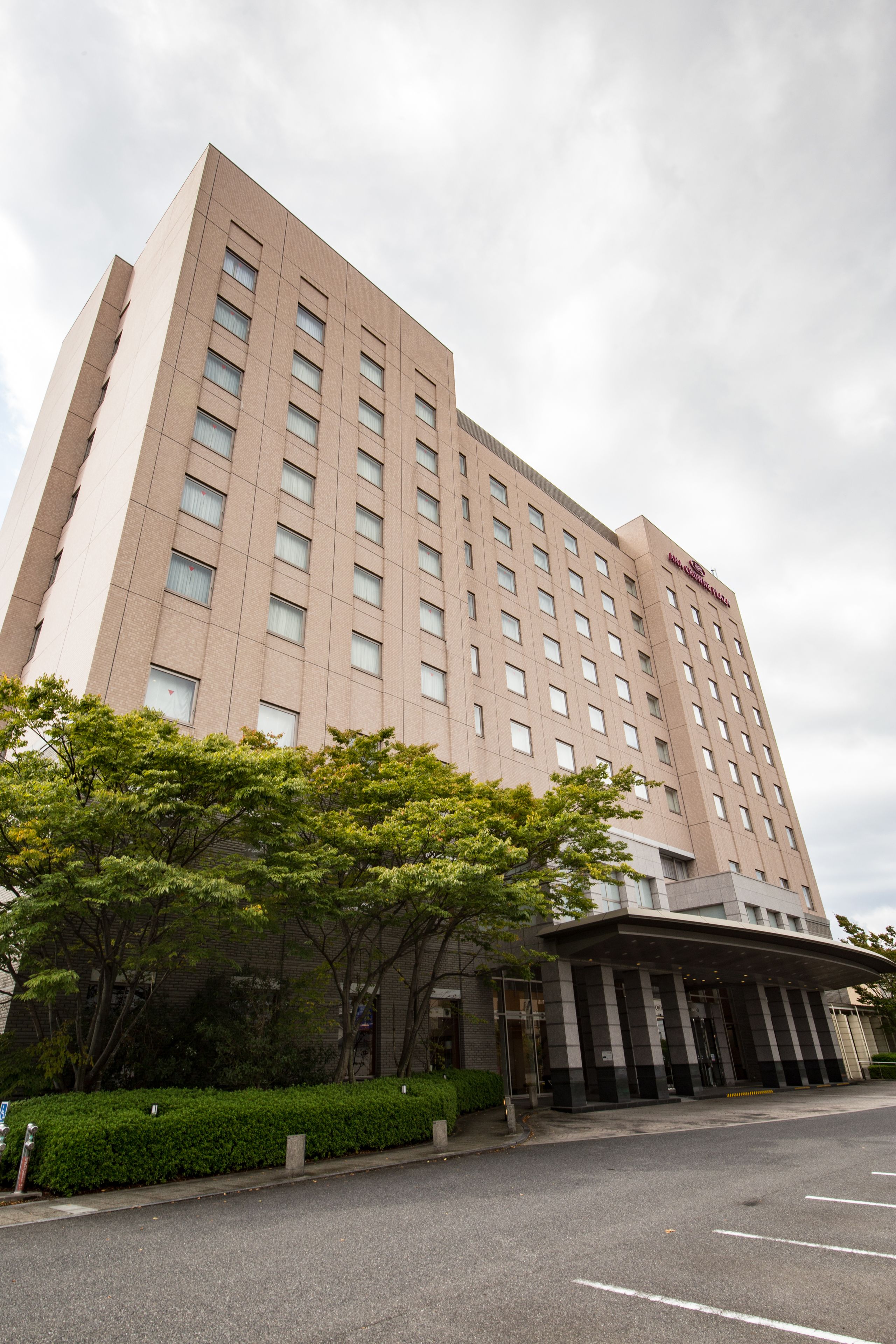 Um hotel alto com design moderno, apresentando uma entrada ampla e área de estacionamento à frente.