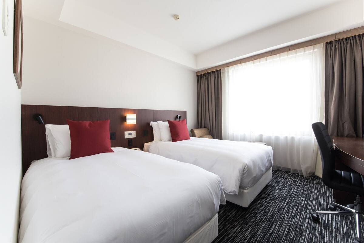 Ein Hotelzimmer mit zwei Betten, einem Schreibtisch und einem Stuhl.