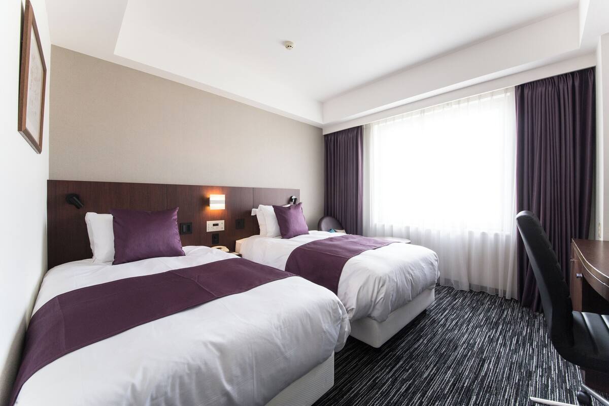 Ein Hotelzimmer mit zwei Betten, einem Schreibtisch und einem Stuhl.