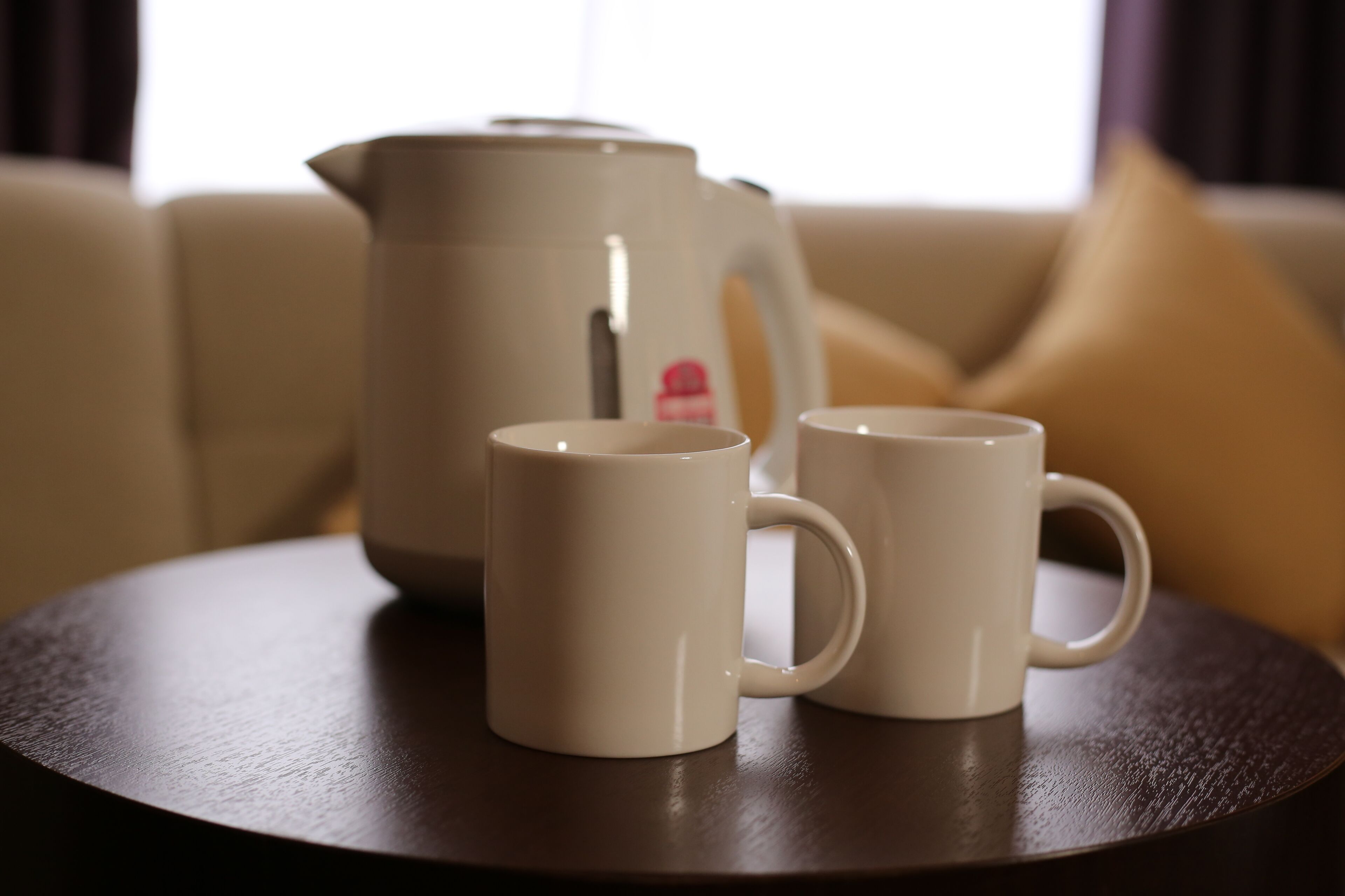 Deux tasses blanches sont posées sur une table ronde, et une cafetière beige se trouve à l’arrière-plan.