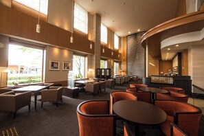 A spacious hotel lobby with multiple seating areas, large windows, and a curved reception desk.