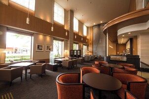 A spacious hotel lobby with multiple seating areas, large windows, and a curved reception desk.