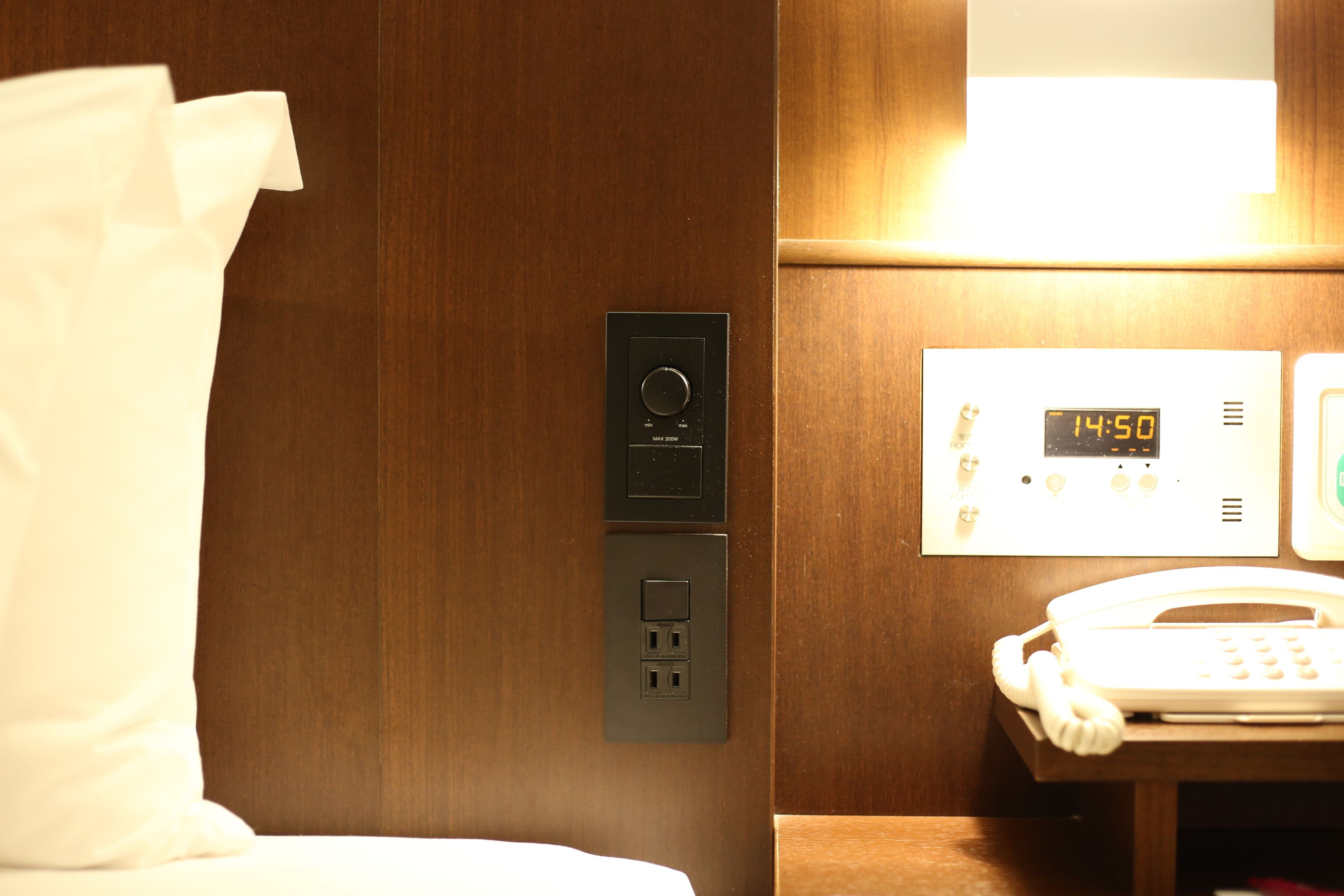 Ein Hotelzimmer mit Bedienfeld, digitaler Uhr und Telefon auf einem Holztisch.