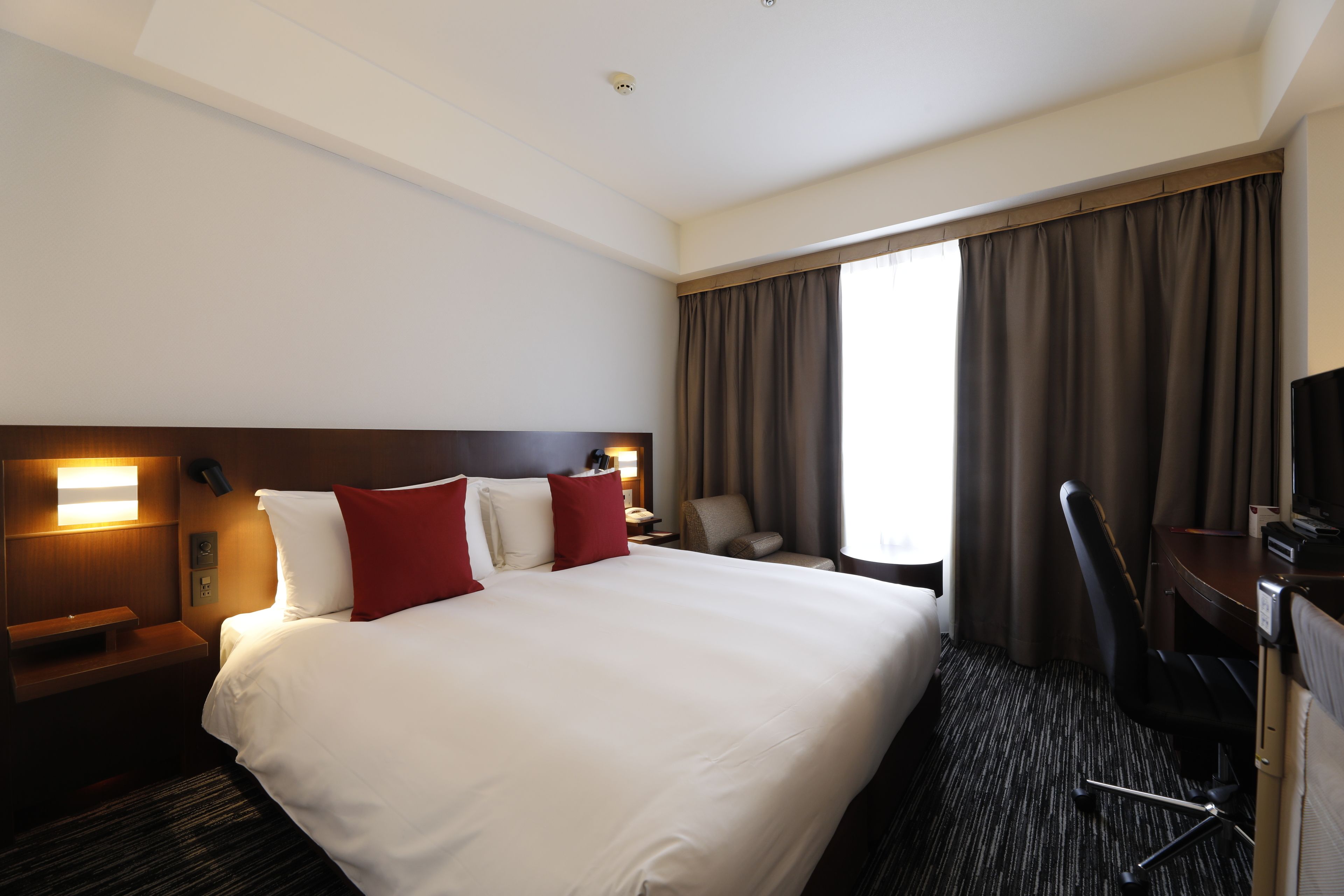 A hotel room with a large bed, a desk with a chair, a TV, and a window with curtains.