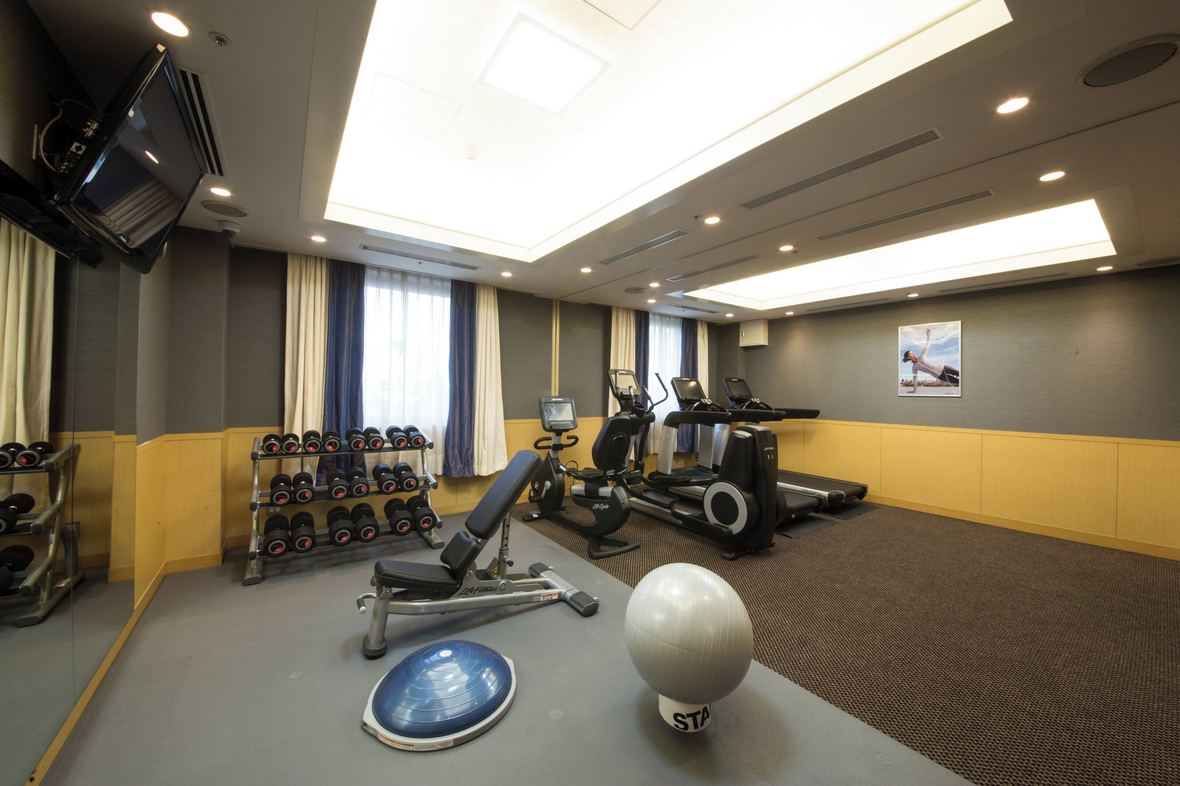 A gym with exercise equipment, a TV, and a large window with curtains.