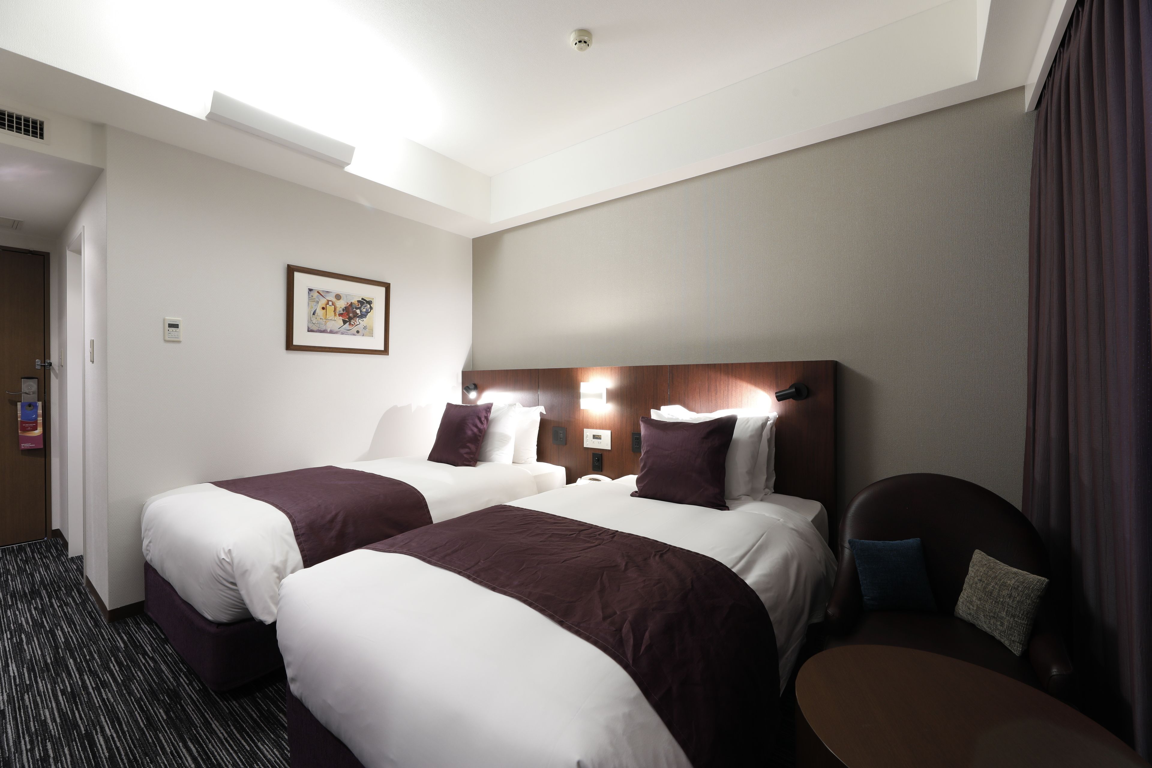 A hotel room with two beds, a wooden headboard, a small table, and a wall-mounted artwork.