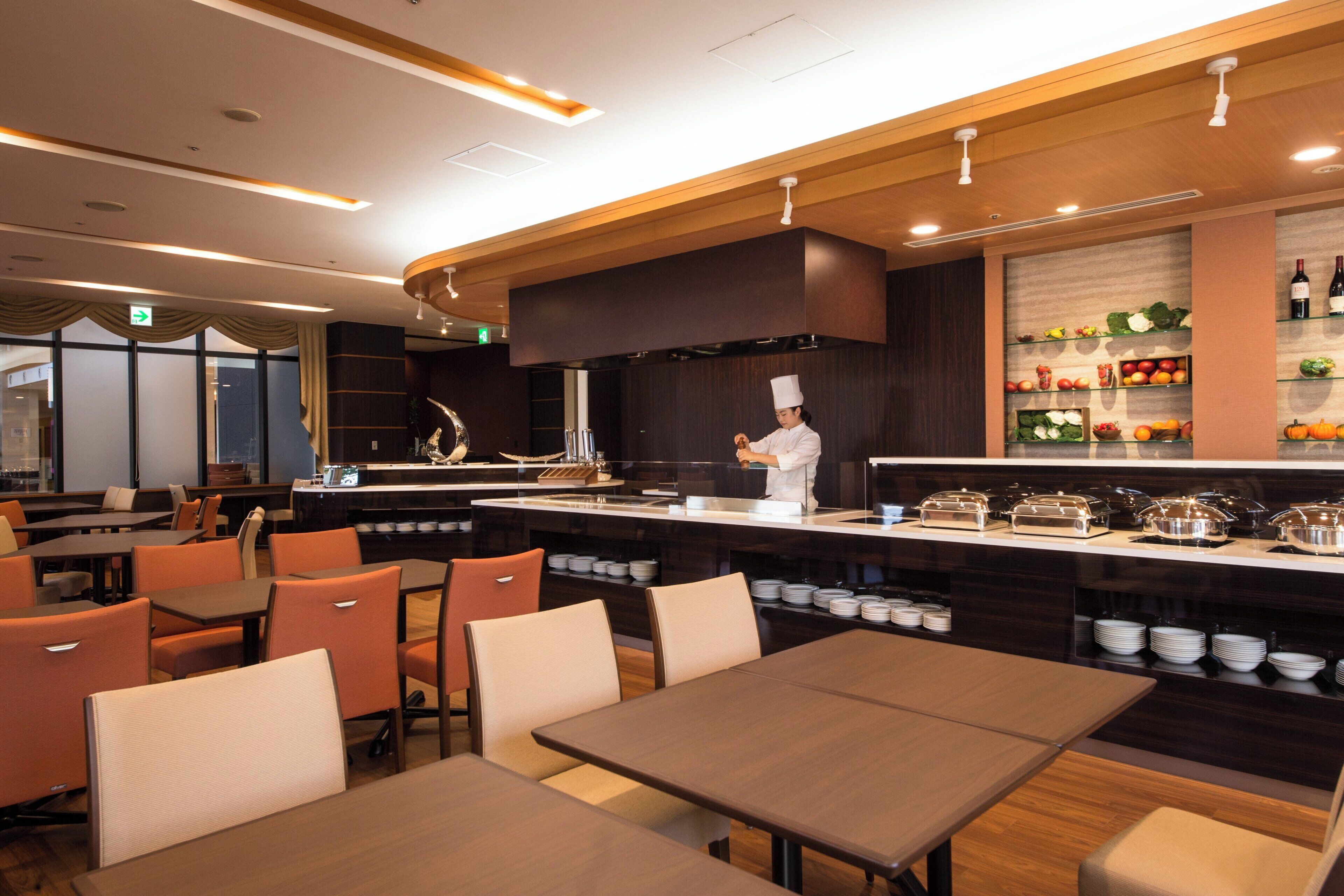 Een restaurant met een kok die eten bereidt, eettafels en een buffet met diverse gerechten.