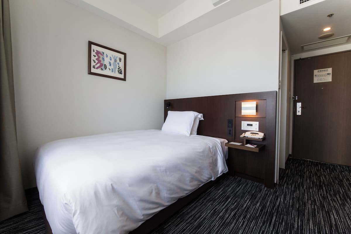 Ein Hotelzimmer mit einem Bett, einem Nachttisch mit Lampe, einem Telefon und einer Tür mit Schild.