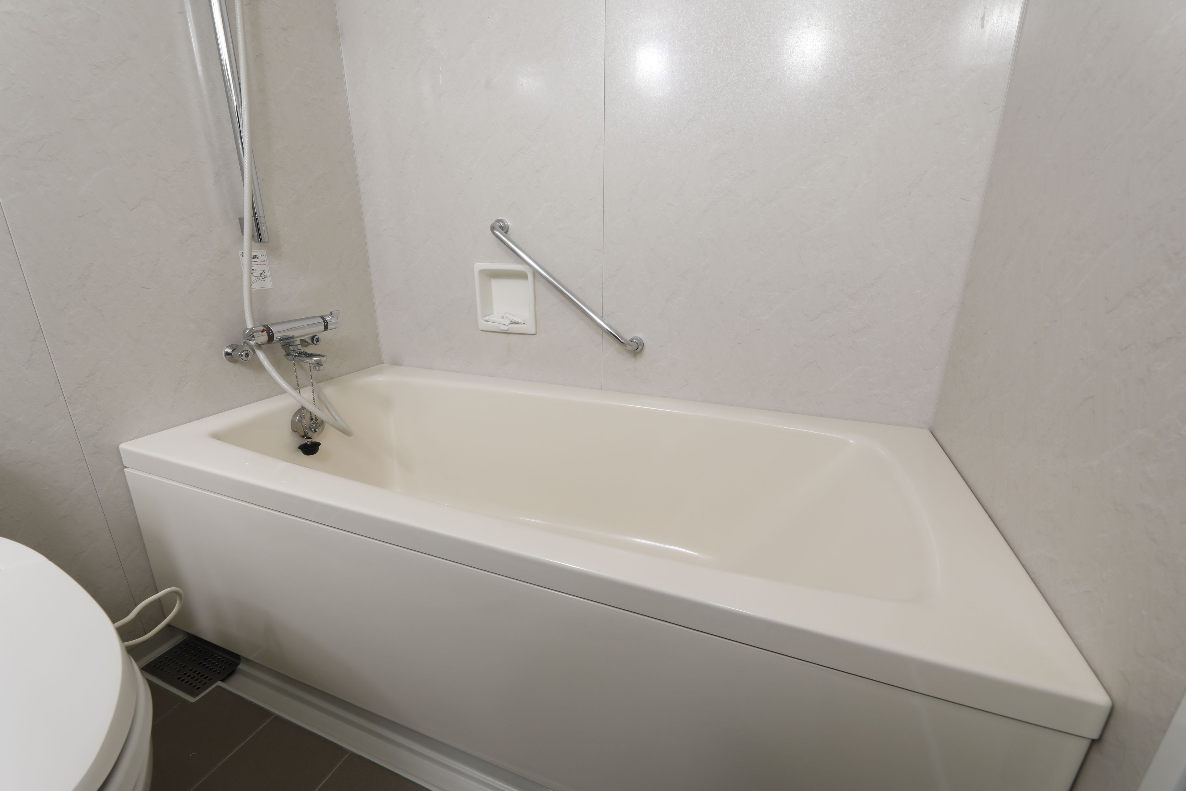 Eine weiße Badewanne mit Duschbrause, Haltegriff und einer kleinen Bedienkonsole.