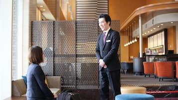 A man and a woman in a hotel lobby with seating areas, a reception desk, and a patterned wall.