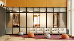 A lobby with a modern design, featuring a seating area with white chairs and orange ottomans, a patterned carpet, and a large window with a view of the interior.