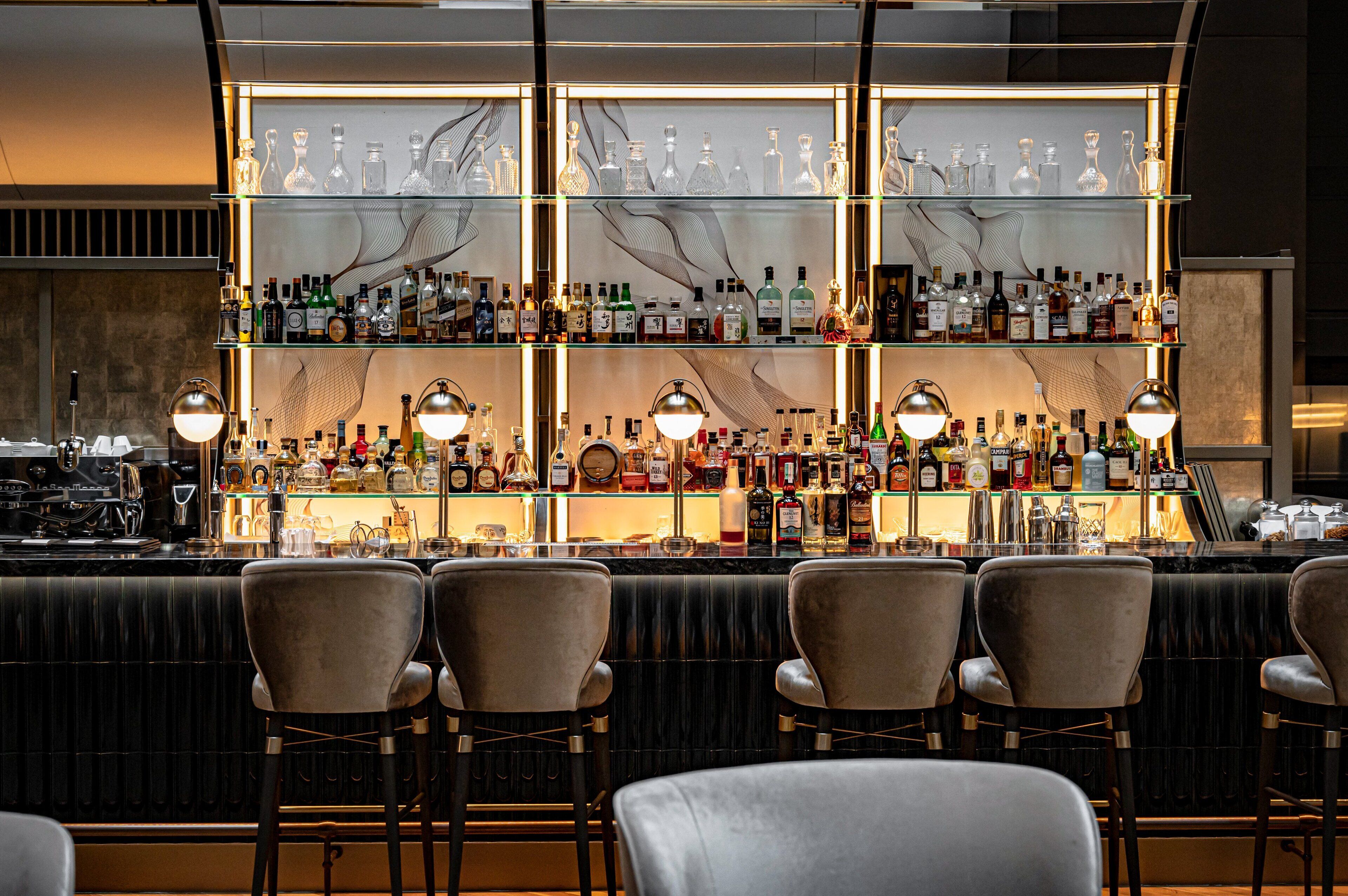 A bar area with multiple shelves of liquor bottles, bar stools, and pendant lighting.