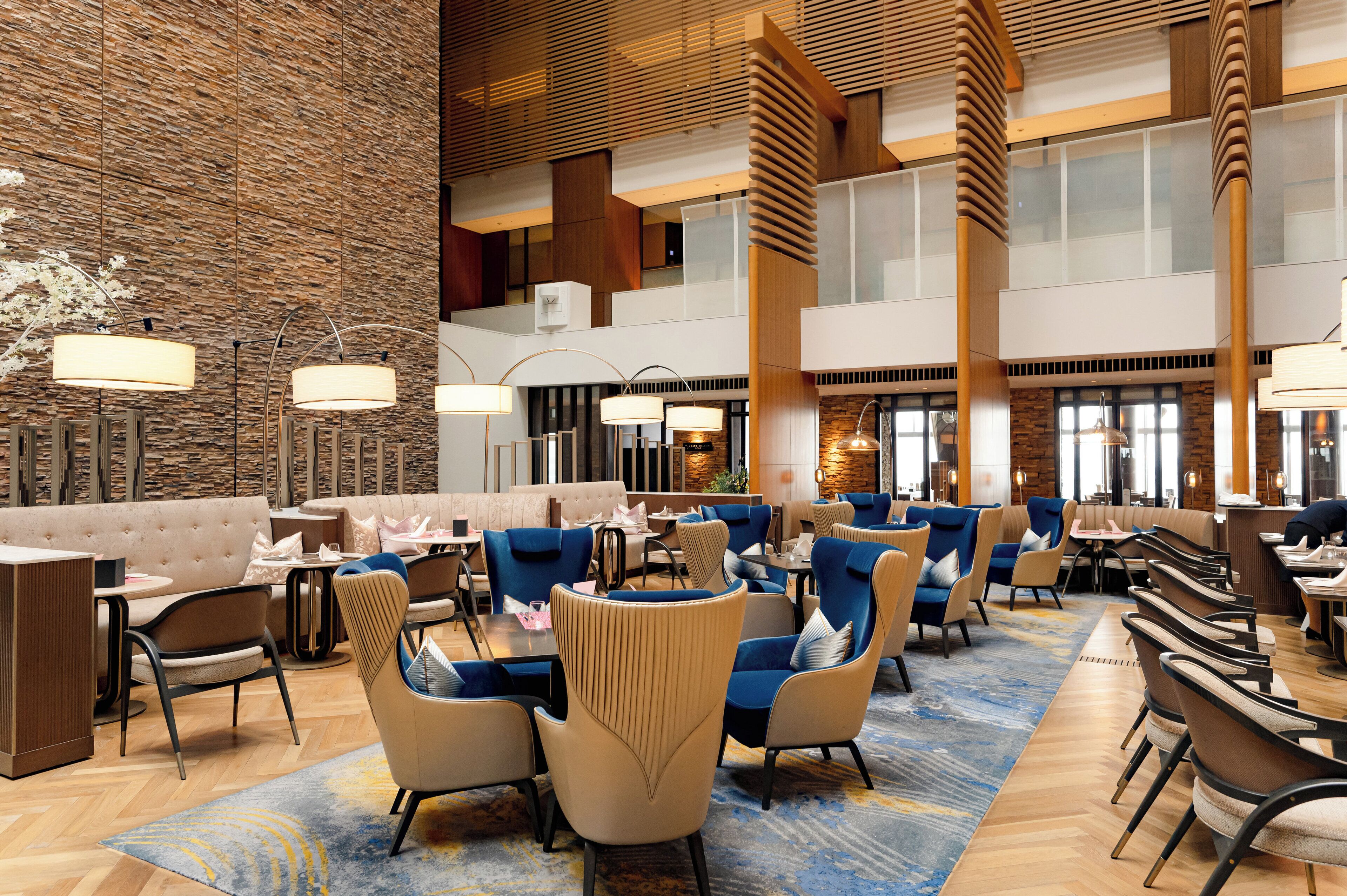 A spacious lobby with a high ceiling, multiple seating areas, and a central fireplace.