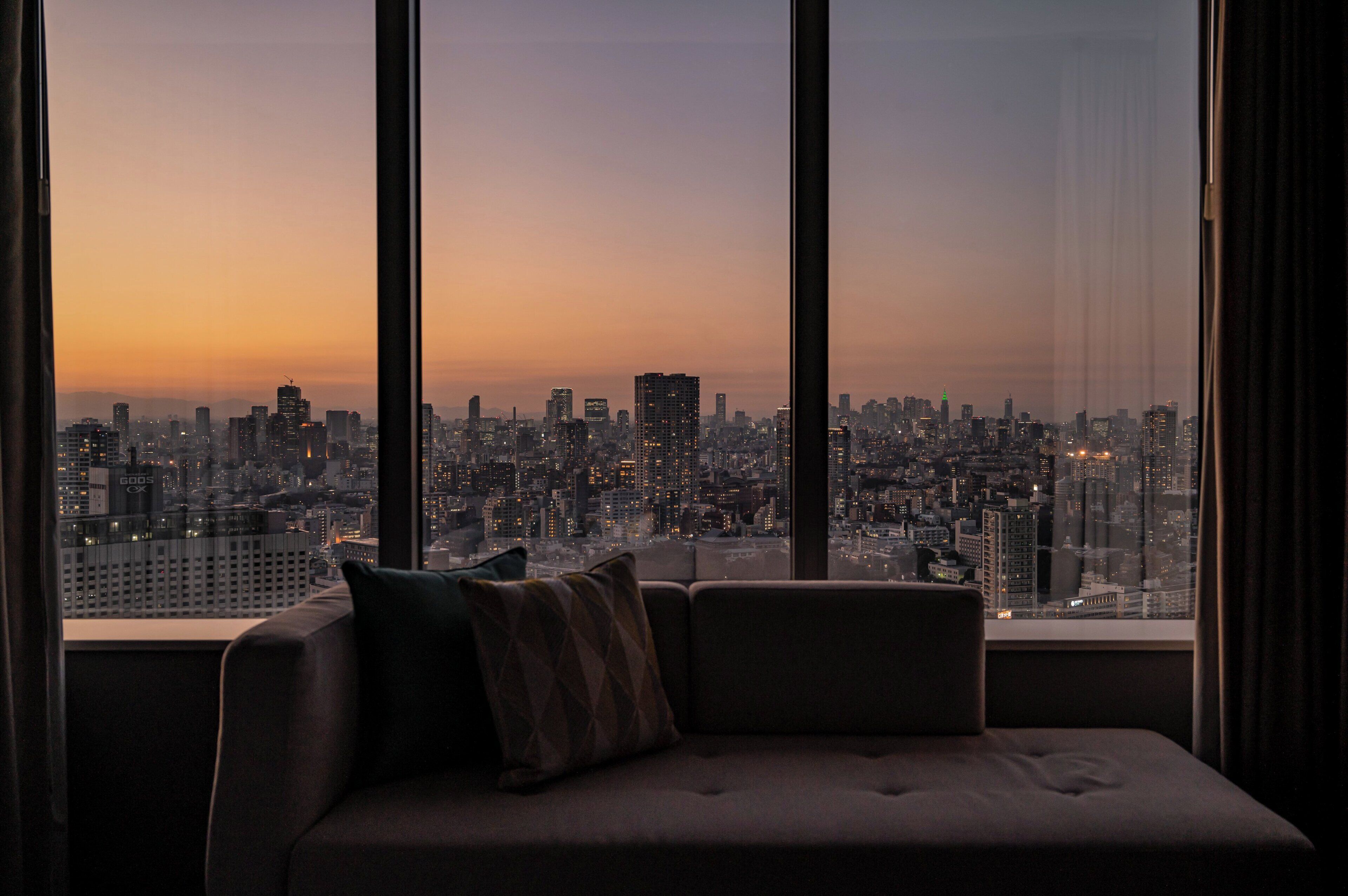 A cityscape view from a high-rise building with a sofa and cushions in the foreground.
