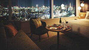 Habitación de hotel con vista a la ciudad, una mesa de comedor con comida y bebidas, un sofá y una lámpara.
