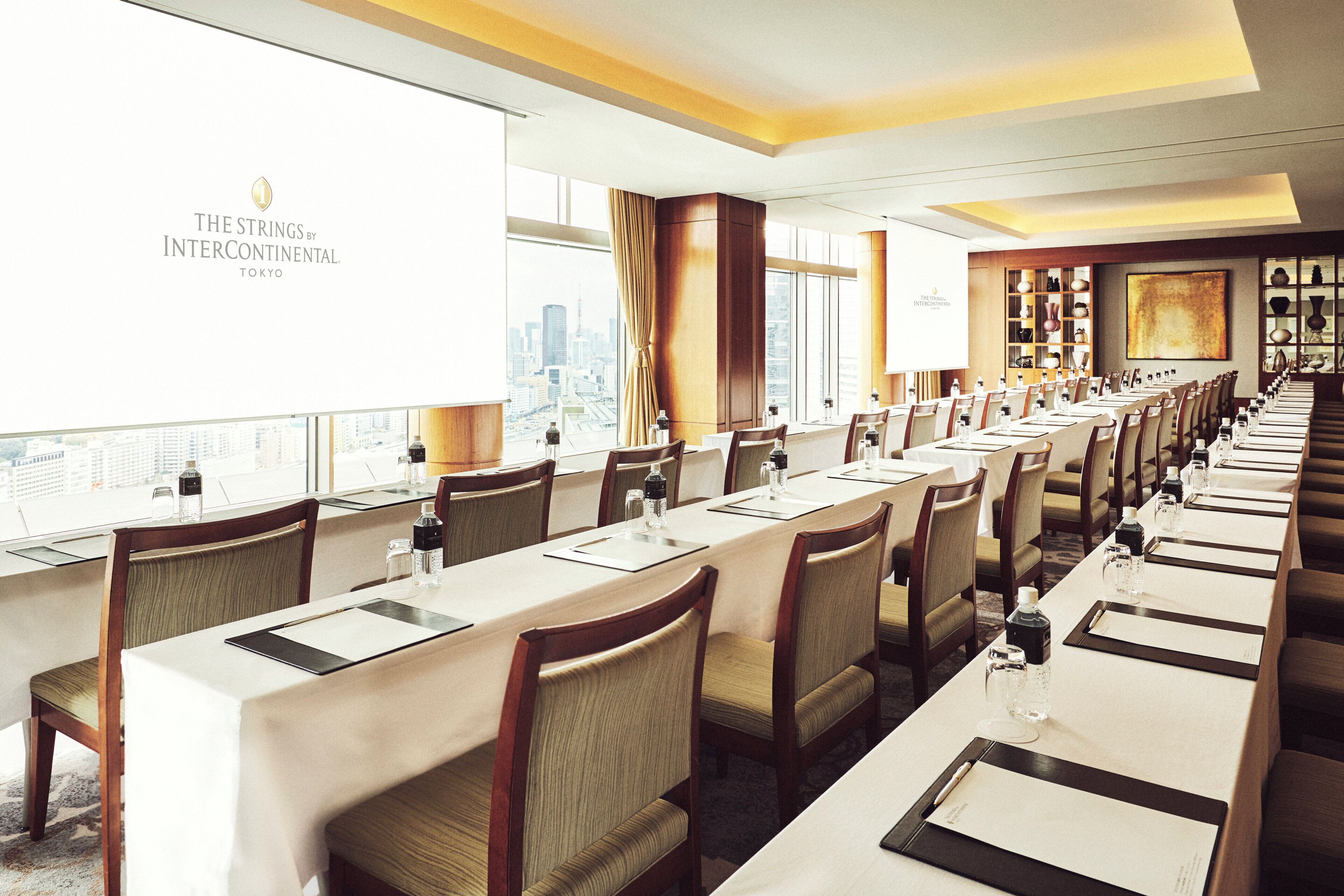 A conference room with long tables, chairs, and a city view.