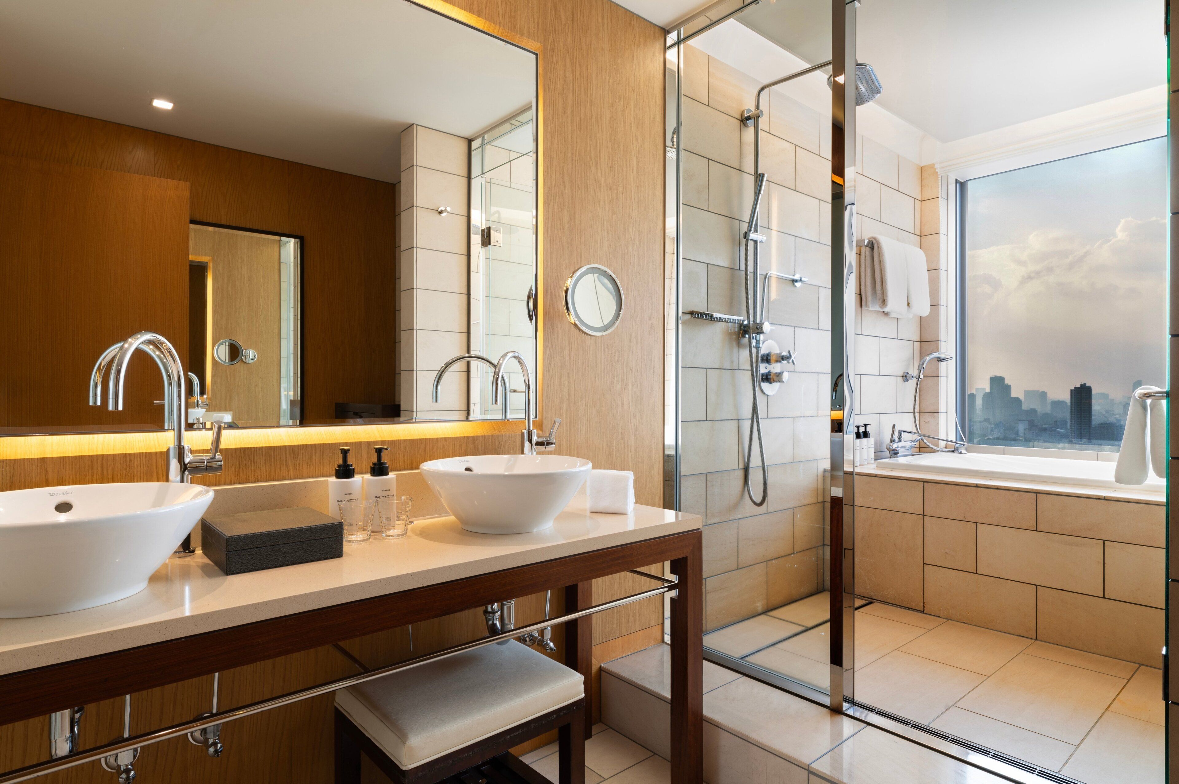 A modern bathroom with two sinks, a shower, and a large mirror.