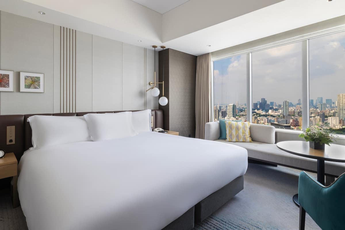 Une chambre d’hôtel avec un grand lit, un canapé, une petite table et une vue sur le paysage urbain.