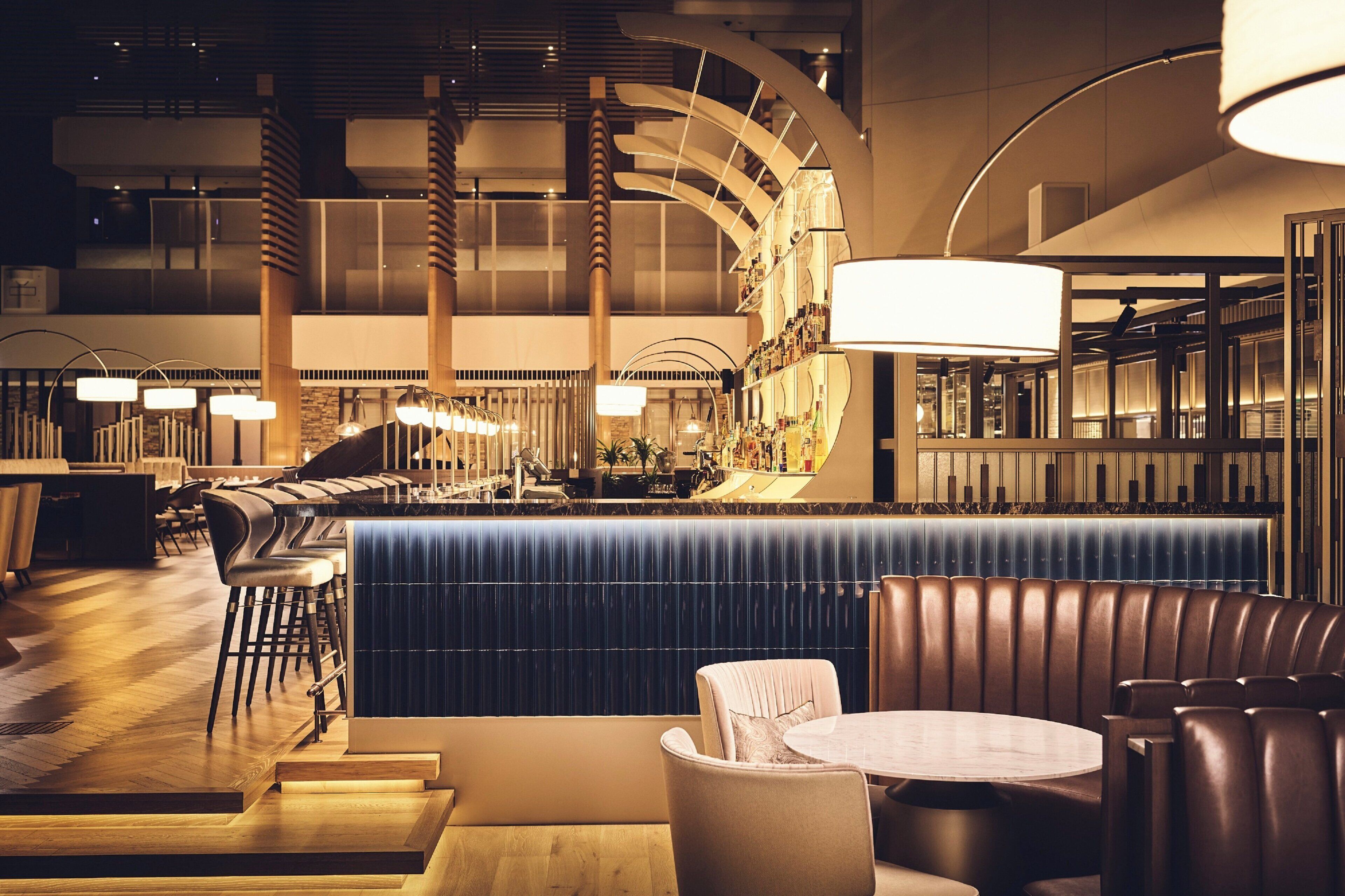 A modern bar area with a curved counter, seating, and a large hanging light fixture.