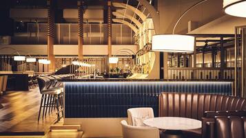 A modern bar area with a curved counter, seating, and a large hanging light fixture.