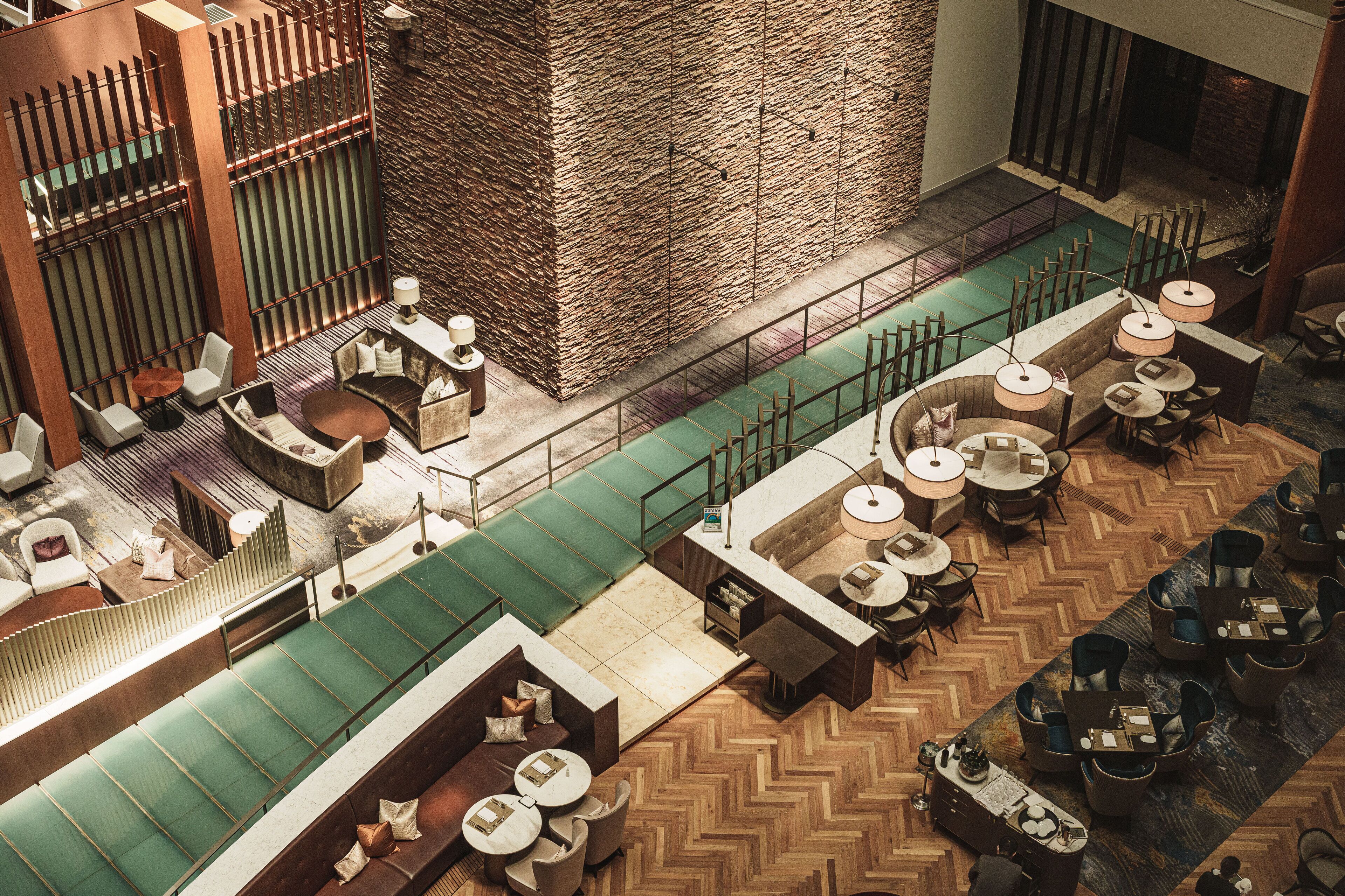 A spacious hotel lobby with a high ceiling, a central seating area, and a large stone wall.