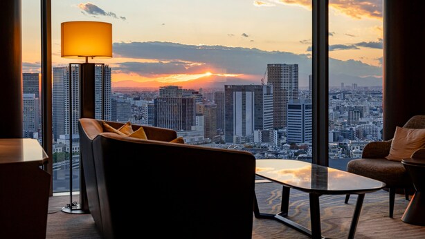 Habitación de hotel moderna con un amplio ventanal que ofrece vistas panorámicas de la ciudad al atardecer.